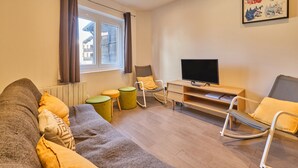 Ett modernt vardagsrum med en soffa, två gungstolar, en tv och ett fönster med gardiner.