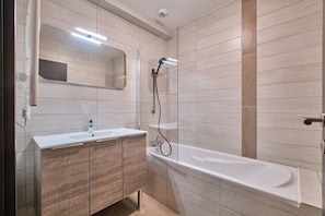 A modern bathroom with a sink, mirror, and bathtub.