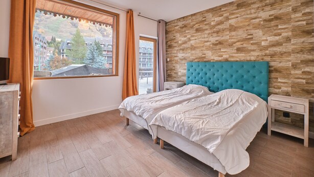 Una camera da letto con una grande finestra, un letto con testiera color acquamarina, una parete in legno e un comodino.