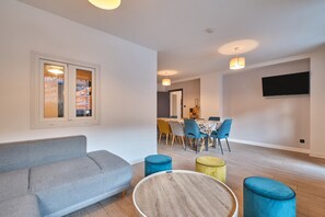 Un salon moderne avec un canapé, une table basse ronde et des poufs. On aperçoit à l’arrière-plan un coin repas avec des chaises et une table.
