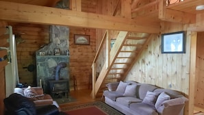 En mysig stuga med en inredning som inkluderar en steneldstad, en soffa, en fåtölj i läder och en trappa.