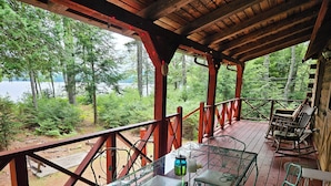 Ett trädäck med ett glasbord och stolar, med utsikt över ett skogsområde och en sjö eller ett annat vattendrag.
