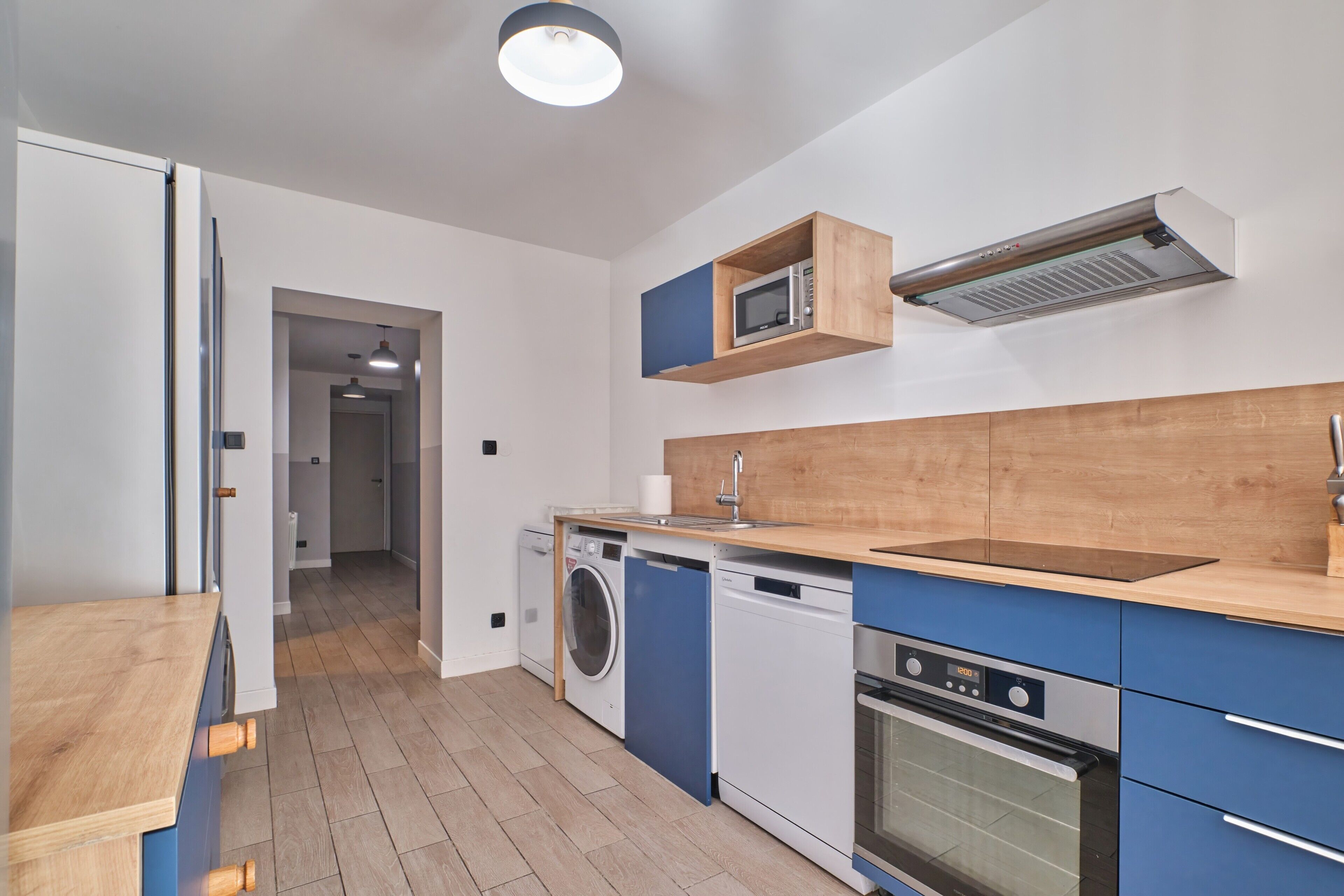 A compact kitchen with a microwave, oven, washing machine, and wooden countertop.
