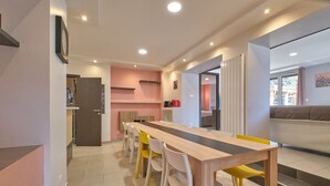 Cozinha moderna com uma mesa de madeira comprida e cadeiras amarelas, uma parede rosa e uma janela com vista.