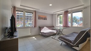 Quarto com cama, mesa, televisão e janelas com cortinas.