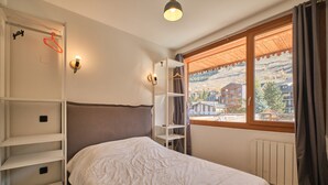 Un dormitorio con cama, armario, estantería y ventana con vistas a edificios.