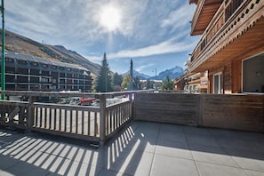Un balcon donnant sur une montagne, un bâtiment en bois et une rue où circulent des véhicules.