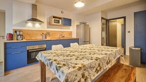 A compact kitchen with a microwave, oven, and sink, a dining table with a floral tablecloth, and a trash can.