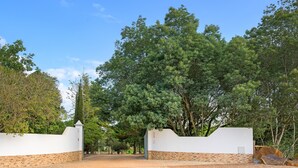 A gated entrance with a white wall and a stone base, surrounded by trees. - Holiday Home 'Sobreirinho - Selão Da Eira' with Sea View, Shared Pool and Wi-Fi (São Teotónio)