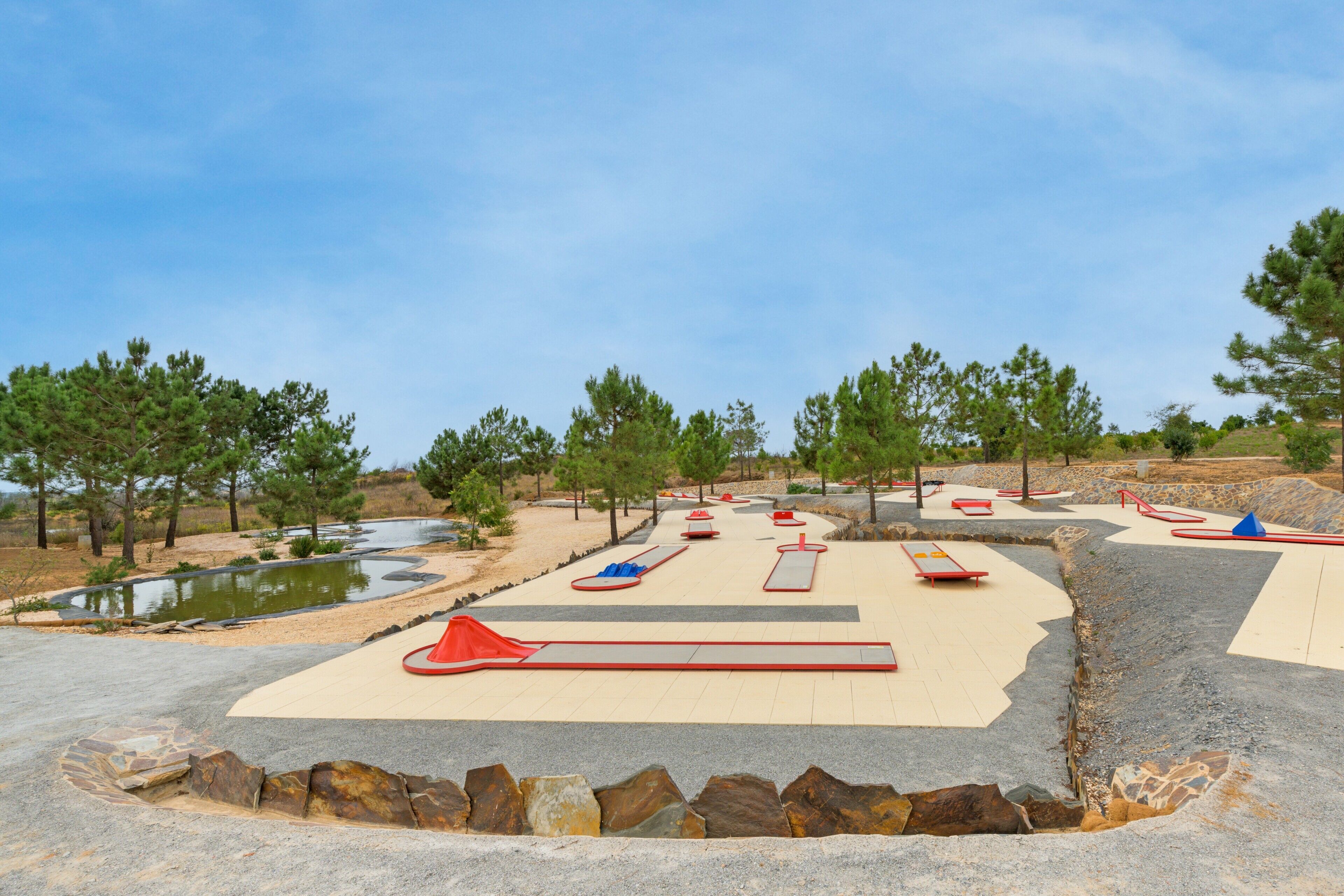 An outdoor play area with slides, a small pond, and surrounding trees.