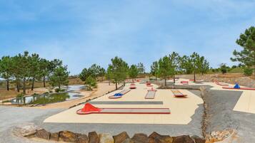 An outdoor play area with slides, a small pond, and surrounding trees.