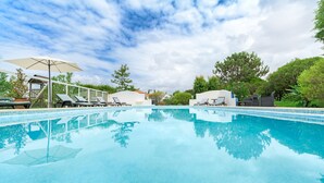 A clear swimming pool with lounge chairs and umbrellas, surrounded by greenery and a wooden fence. - Holiday Home 'Casa Alecrim - Selão Da Eira' with Sea View, Wi-Fi & Air Conditioning (S.Teotónio)