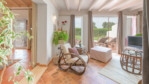 A spacious room with a wicker rocking chair, a glass table, and a television. - Holiday Home 'Casa Alecrim - Selão Da Eira' with Sea View, Wi-Fi & Air Conditioning (S.Teotónio)