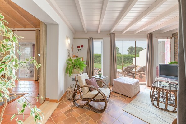 A spacious room with a wicker rocking chair, a glass table, and a television.