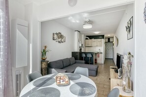 A modern living room with a grey sectional sofa, a dining table with placemats, a kitchen in the background, and a decorative vase on a side table.
