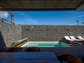 Zona de piscina amb gandules, una paret de pedra i un pont de fusta.