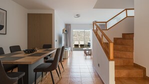 A modern interior with a dining area, a staircase, and a view to an outdoor space.