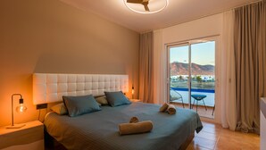A bedroom with a large bed, a bedside table with a lamp, a ceiling fan, and a view of the outdoors through a sliding glass door.