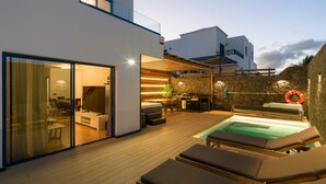 A modern outdoor living area with a pool, lounge chairs, a dining area, and a stone wall.