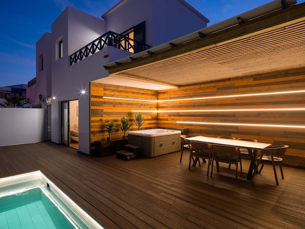 Une terrasse extérieure moderne dotée d’une piscine, d’une plateforme en bois et d’un espace repas avec un jacuzzi.