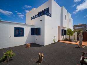Un bâtiment moderne aux murs blancs et aux volets bleus, un petit jardin agrémenté d’un cactus, et une enseigne indiquant le « Centre d’affaires de Playa Blanca ».
