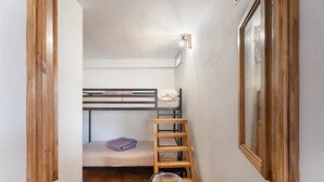 Um quarto pequeno com beliche, escada de madeira, janela e espelho.