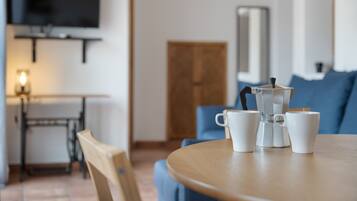 Een ronde tafel met een koffiezetapparaat en kopjes, een televisie aan de muur en een deur op de achtergrond.