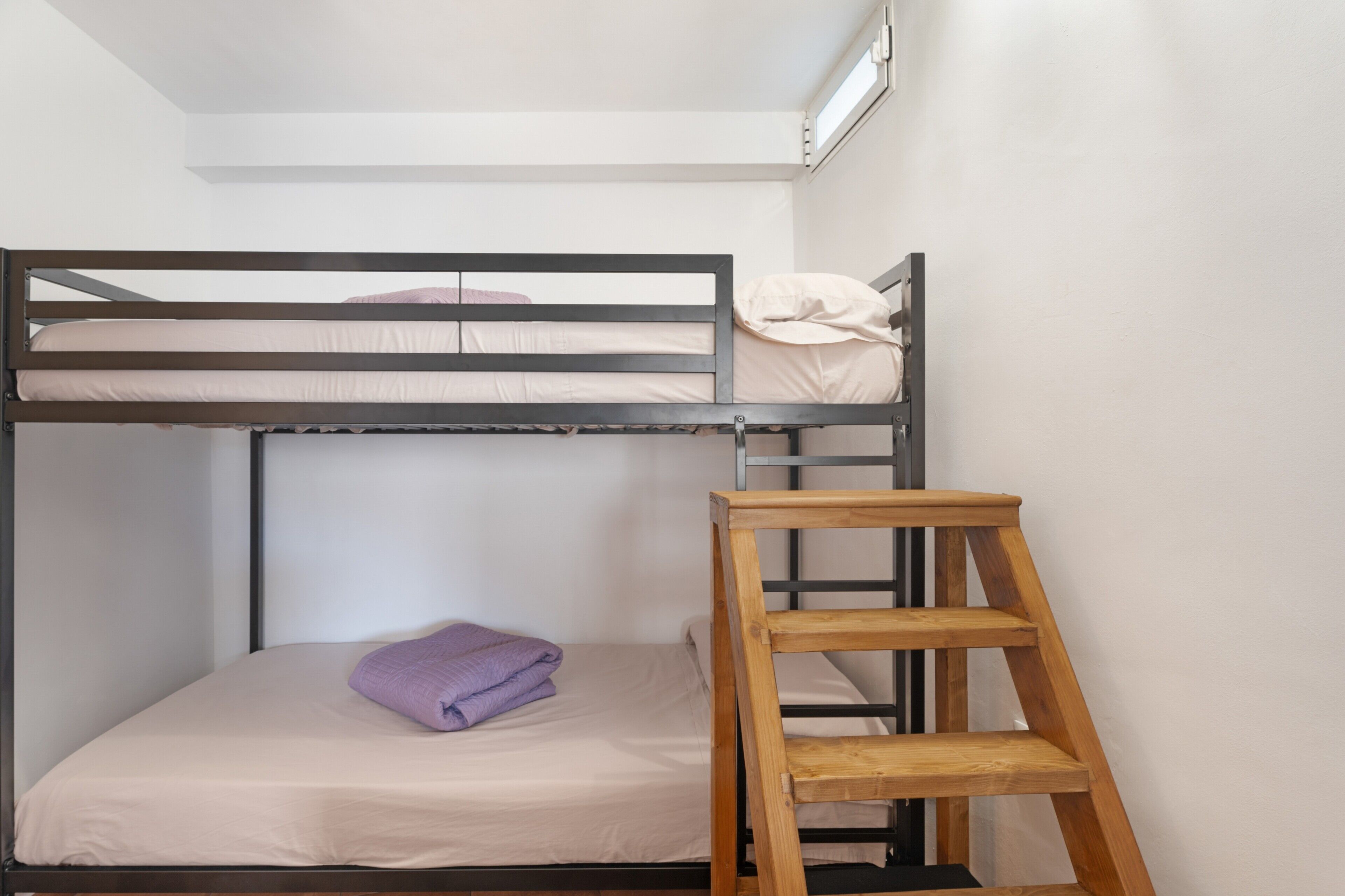 Een stapelbed met een houten ladder, een enkel bed beneden en een raam erboven.