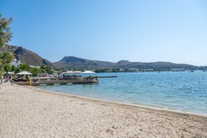 A beach with a pier, mountains in the background, and a clear sky. - Apartment 'Boquer' with Shared Pool, 2 Private Terraces and Wi-Fi (Pollença)