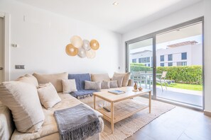 Un saló modern amb un sofà, una taula de centre i un gran finestral corredís que dona a una zona exterior.