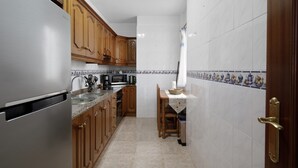 Eine kleine Küche mit Holzausstattung, einem Edelstahlkühlschrank, einer Mikrowelle und einer Kaffeemaschine.
