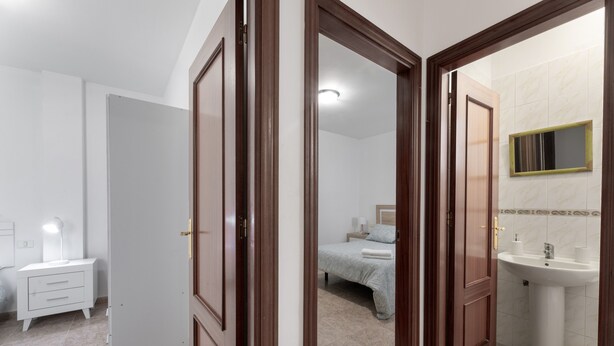 Ein Hotelzimmer mit Bett, Nachttisch und einem Badezimmer mit Waschbecken und Spiegel.