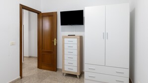 Ein Zimmer mit Holztür, einem weißen Schrank mit Schubladen, einem darüber montierten Fernseher und einem großen, weißen Kleiderschrank.