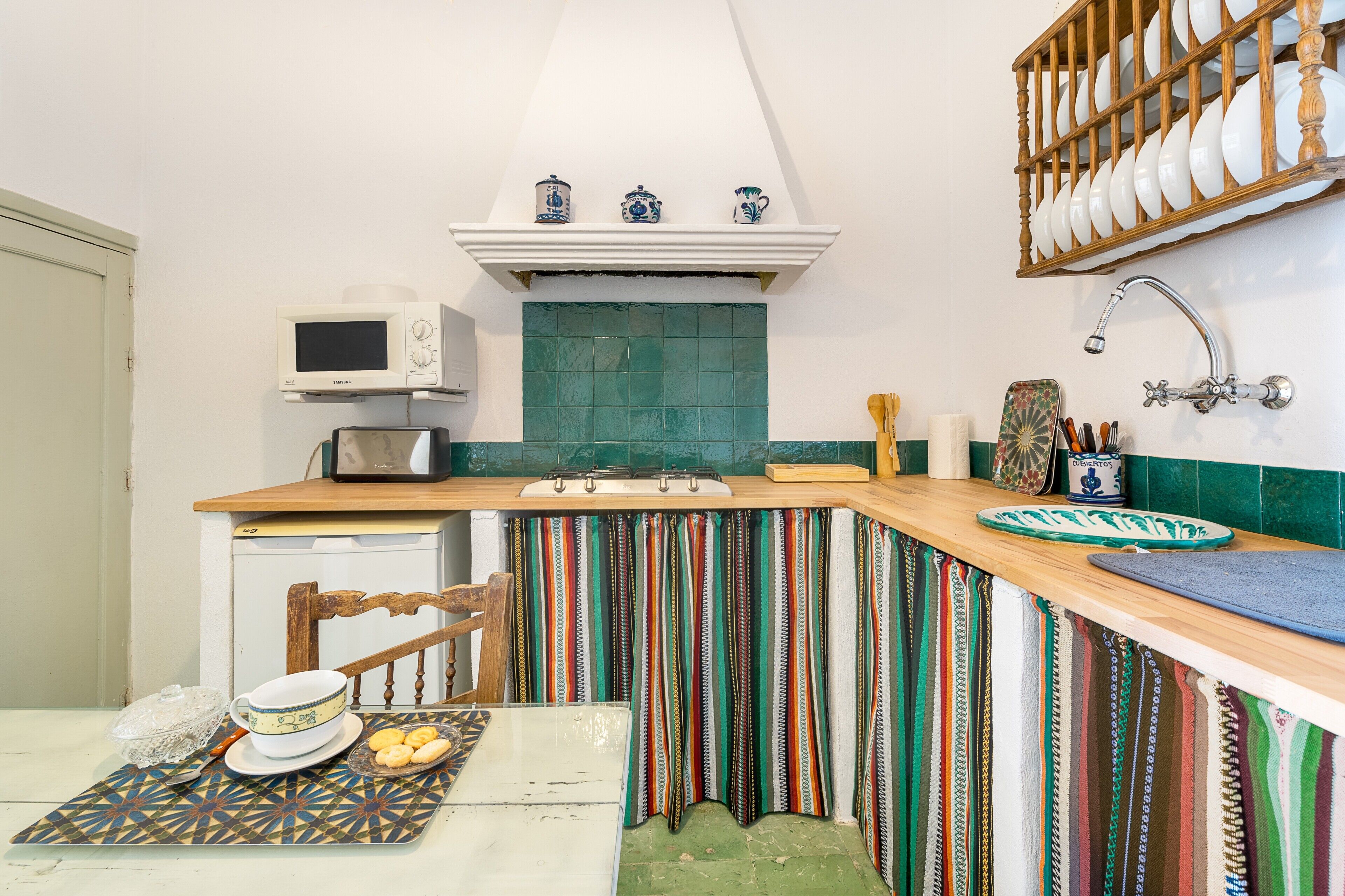 A kitchen with a microwave, a sink, a wooden countertop, and a chair.