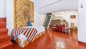 Un dormitorio con cama, un tapiz grande, una escalera, un comedor y vistas al exterior.