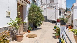 Una calle estrecha con edificios blancos, plantas en macetas y una puerta pequeña.