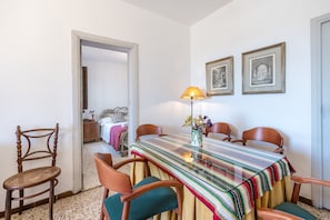 A dining area with a table, chairs, a lamp, and framed pictures on the wall.