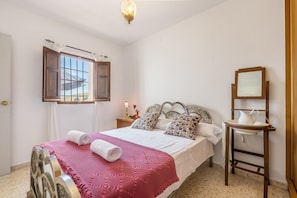 A bedroom with a bed, a nightstand, a bedside table, a mirror, and a window with curtains.