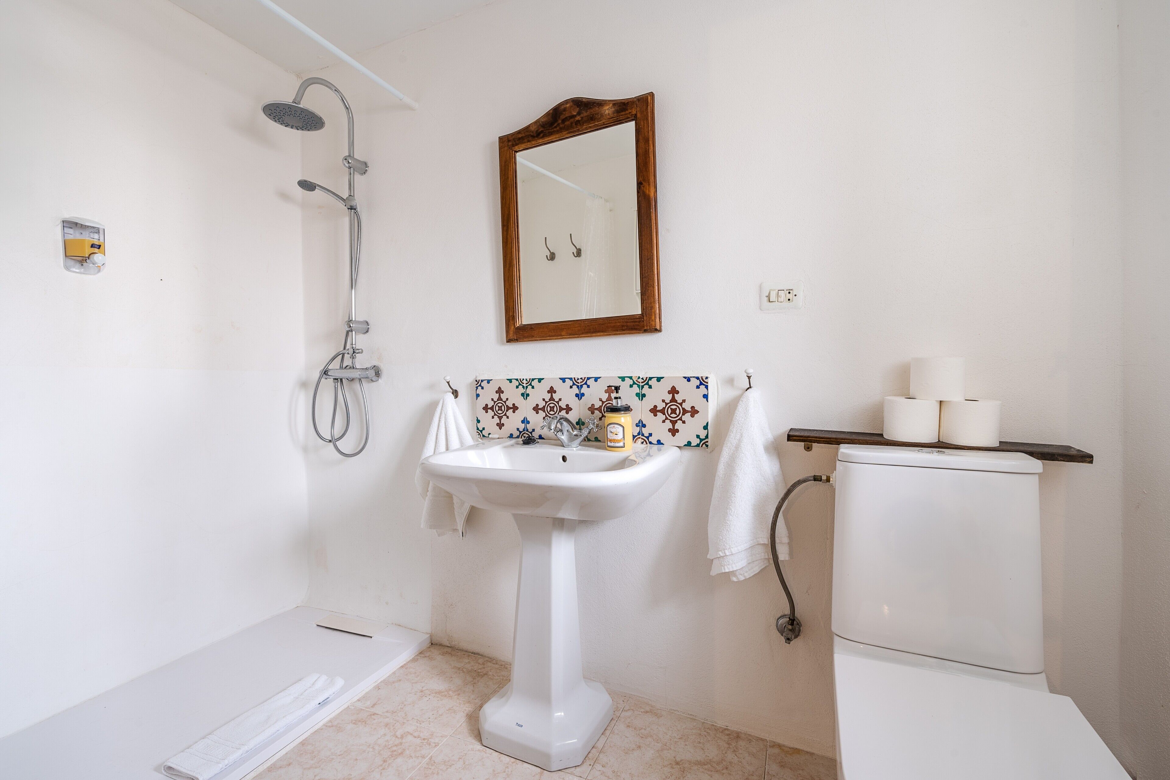 Un bany amb un lavabo de pedestal, dutxa, vàter i mirall.