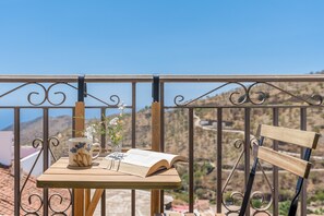 A balcony with a table, an open book, a mug, and a vase with flowers.
