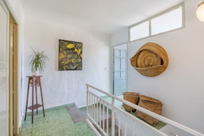A hallway with a green patterned floor, a wooden plant stand, a painting, and woven baskets on a white wall.