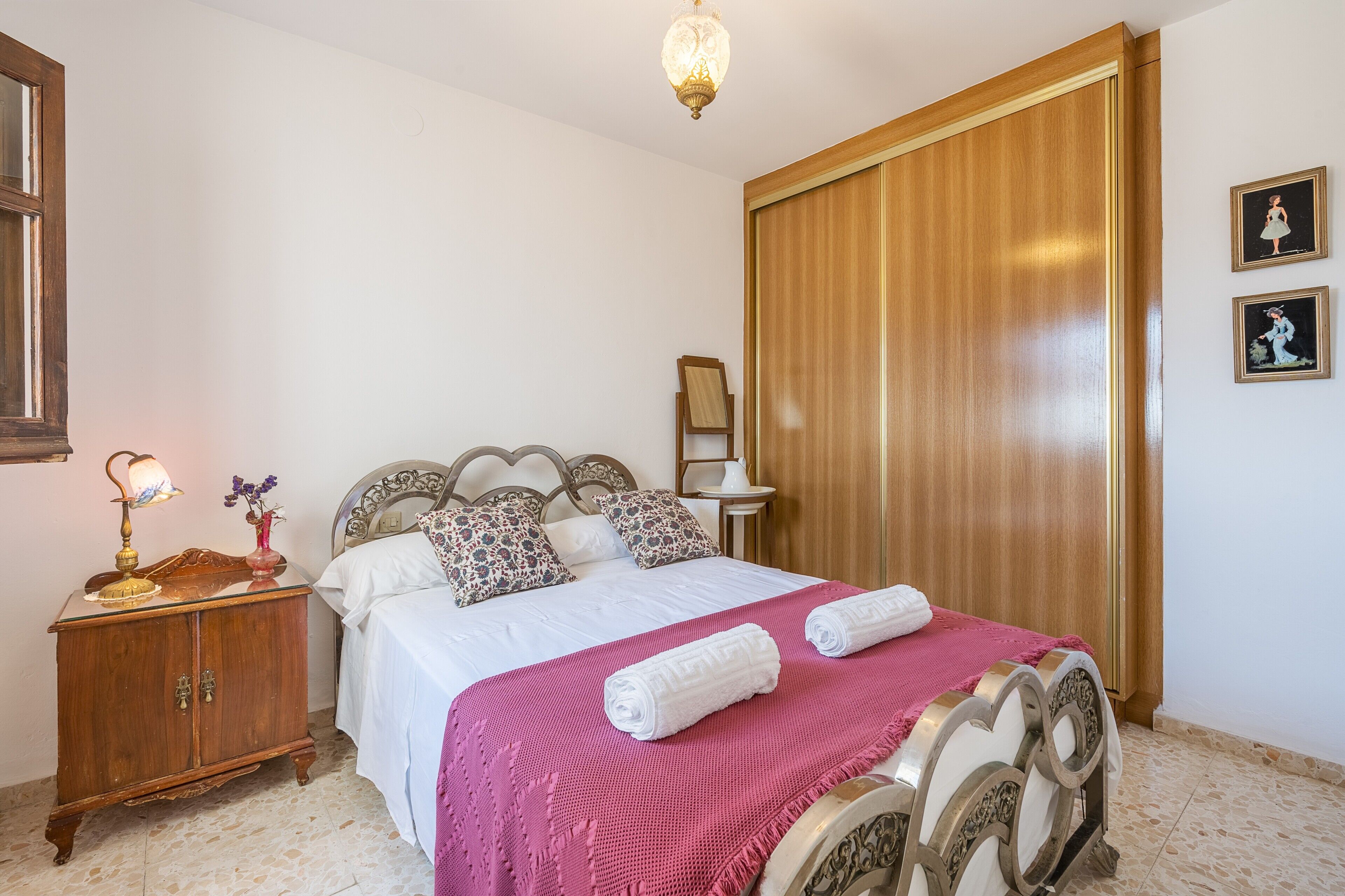 Une chambre à coucher comprenant un lit, une armoire en bois, une table de chevet avec une lampe et des tableaux accrochés au mur.