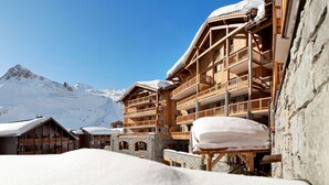 Eine Holzhütte mit Balkonen und einer Steinfassade vor einer verschneiten Berglandschaft.