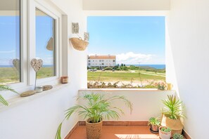 A balcony with potted plants, a view of a building, and a clear sky.