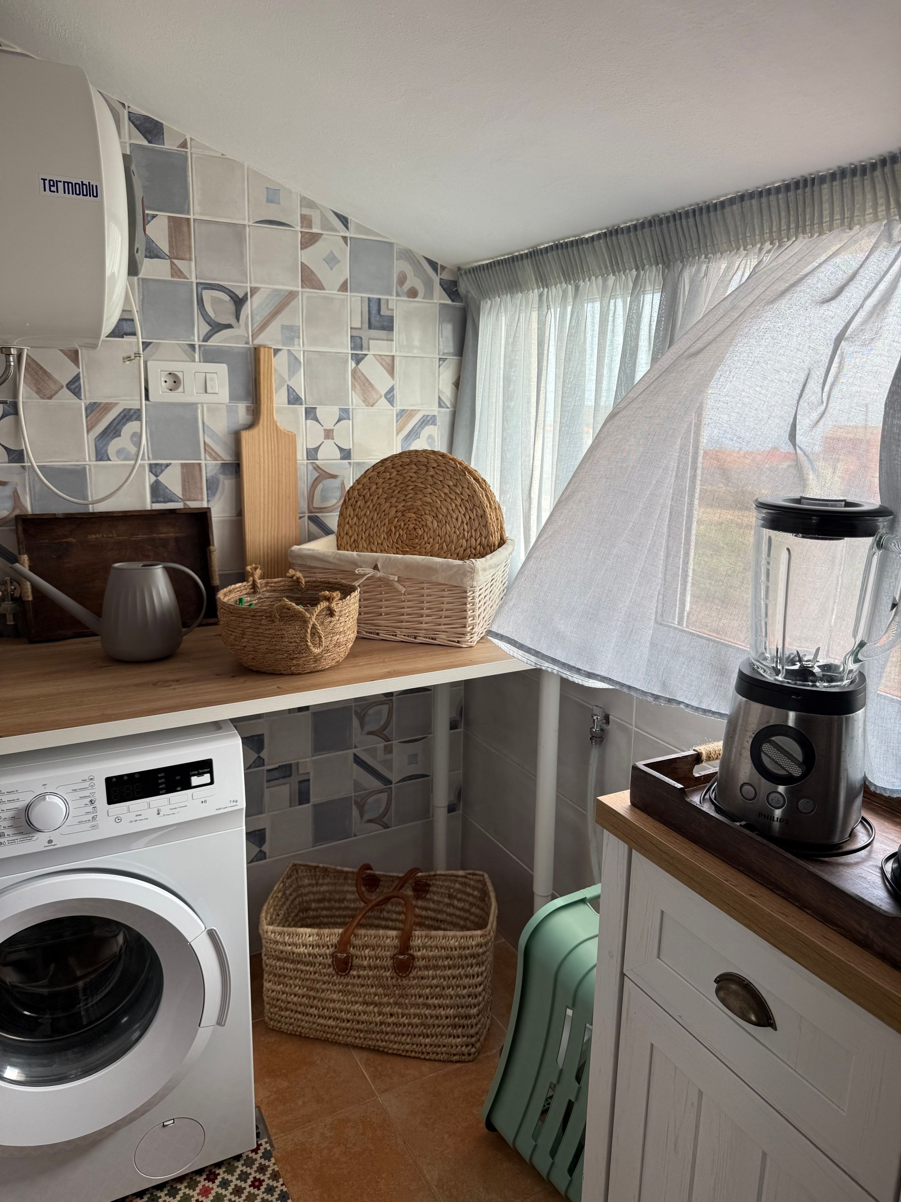 A compact kitchen with a washing machine, a blender, and wicker baskets on the counter.