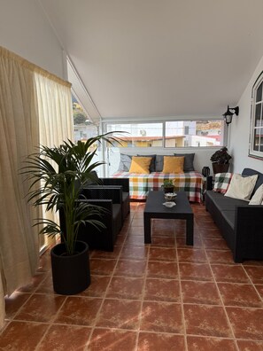Una habitación iluminada por el sol con un sofá a cuadros, una mesa de centro negra y una planta en maceta.