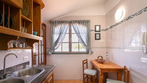 Eine Küche mit Granitarbeitsplatte, Spüle aus Edelstahl, Holzschränken, einem Fenster mit leichtem Vorhang und einer gefliesten Spritzschutzwand.