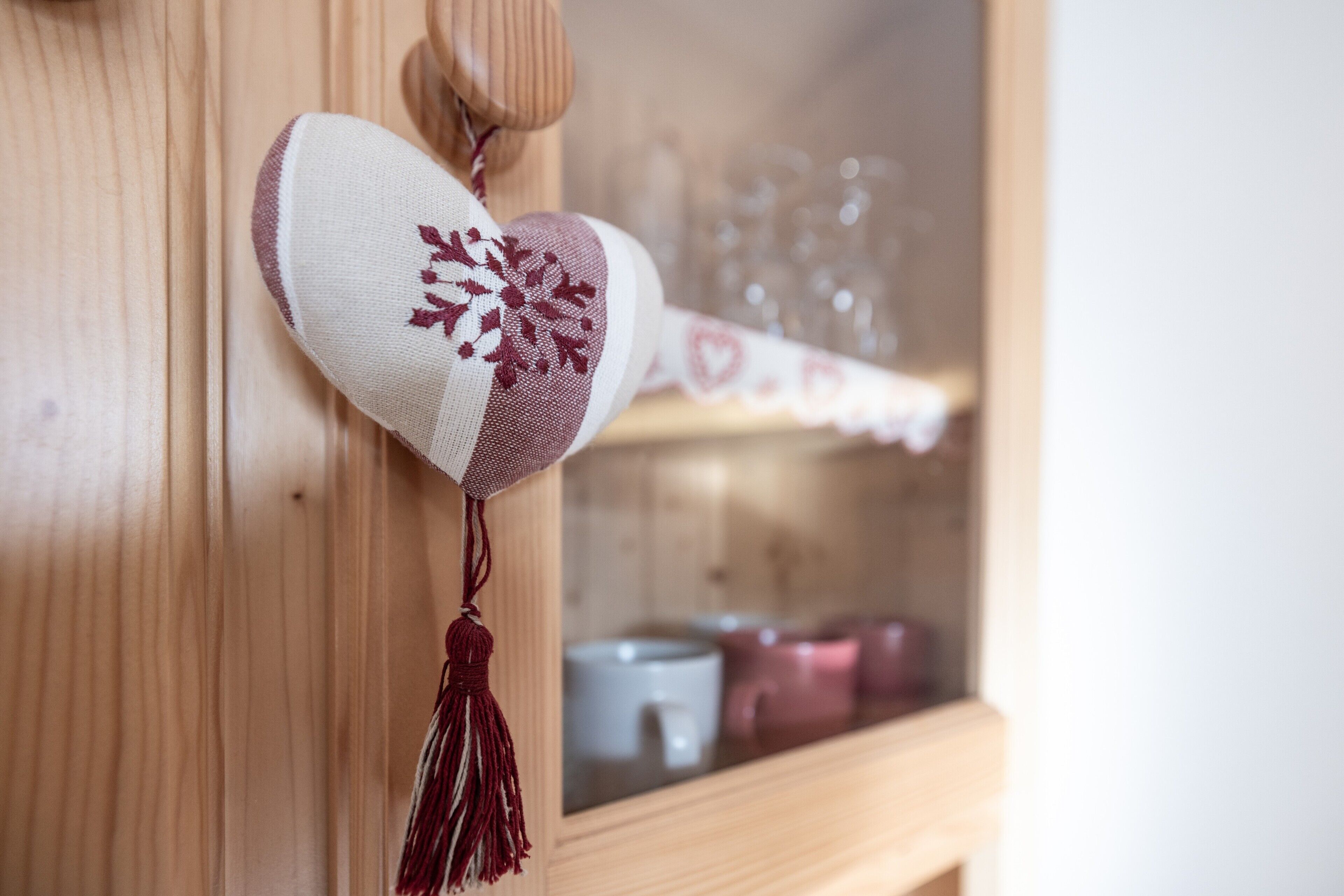Un mueble de madera con puerta de cristal, un cojín con forma de corazón y borla, y una repisa con cristalería y velas.