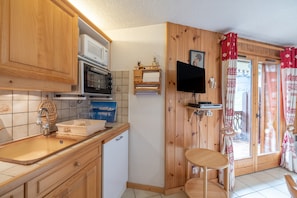 A kitchen with wooden cabinets, a microwave, a sink, and a television mounted on the wall. - Apartment 'L'Ourson 22 - 4-6 People - Morillon' with Mountain View and Balcony (Morillon)