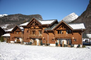 A wooden lodge with balconies, a covered entrance, and a view of snow-covered mountains. - Apartment 'Les Fermes De Samoëns' with Mountain View, Shared Pool and Balcony (Samoëns)